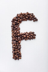 F character made of dark roasted coffee beans on white aquarelle paper background