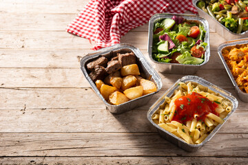 Take away healthy food in foil boxes on wooden table. Copy space	