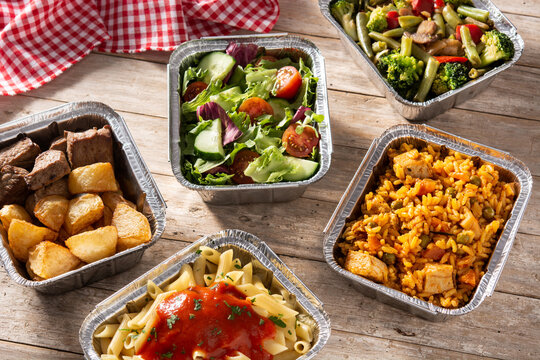 Take away healthy food in foil boxes on wooden table. 