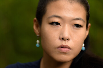 Close-up portrait of beautiful rebel Asian woman face looking serious while thinking outdoors