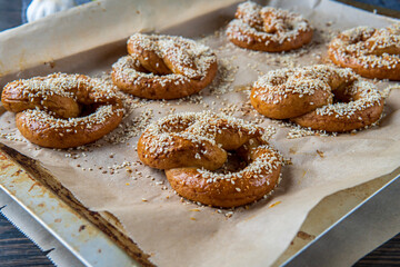 Freshly baked homemade soft pretzels with sesame seeds and garlic flakes, ready to eat. Tasty gluten free savory pastry with a knot placed in a baking tray, hot from the oven.
