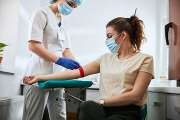 Experienced phlebotomist preparing a woman for blood draw - obrazy, fototapety, plakaty