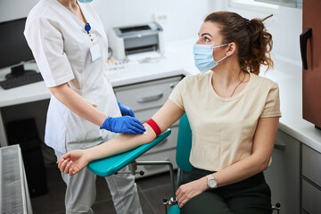 Woman in a medical mask being prepared for venipuncture