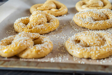 Close up on homemade unbaked soft pretzels with sesame seeds ready to go to the oven on a baking sheet. Gluten free dough for a savory delicious pastry with a knot. Selective focus, side view.