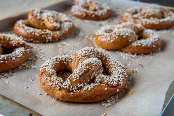 Closeup on a freshly baked homemade soft pretzel with sesame seeds and garlic flakes, ready to eat. Tasty gluten free savory pastry with a knot placed in a baking tray, hot from the oven.