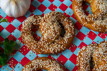 Freshly baked homemade soft pretzels with sesame seeds and garlic flakes, ready to eat. Tasty gluten free savory pastry with a knot on a fun, colorful, background. Coriander and garlic knob aside.