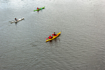 Four people on three kayaks are floating on a calm river. Several people are paddling a kayak....