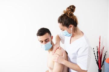 Female physiotherapist treating a patient in a rehabilitation center while wearing a face mask. Working during Coronavirus pandemic concept.