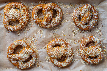 Freshly baked homemade soft pretzels with sesame seeds and garlic flakes, ready to eat and placed on a baking tray. Tasty gluten free savory pastry with a knot. Top view.