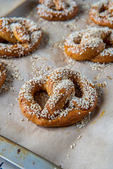 Selective focus on a freshly baked homemade soft pretzel with sesame seeds and garlic flakes, ready to eat. Tasty gluten free savory pastry with a knot placed in a baking tray, hot from the oven.