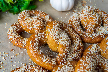 Freshly baked homemade soft pretzels with sesame seeds and garlic flakes, ready to eat. Tasty gluten free savory pastry with a knot on a baking sheet. Coriander and garlic knob in background. Closeup