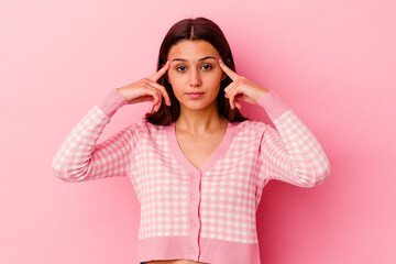 Young Indian woman isolated on pink background focused on a task, keeping forefingers pointing head.