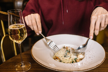 Person eating pasta with shrimps and drinking sparkling wine.