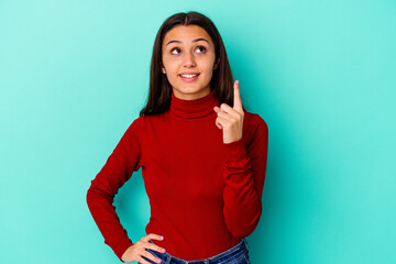 Young Indian woman isolated on blue background indicates with both fore fingers up showing a blank...