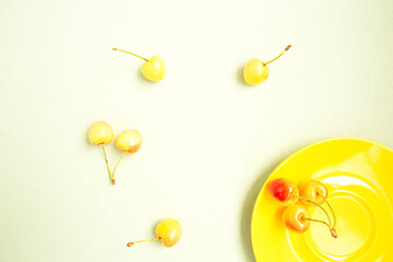 Ripe, yellow cherries on a yellow plate on a light background. Fresh fruits