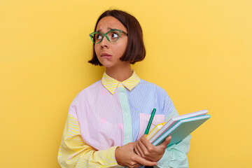 Young mixed race student woman isolated on yellow background confused, feels doubtful and unsure.