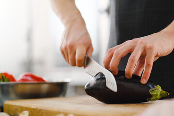 The male Caucasian chef cuts vegetables, peppers, tomatoes and eggplants on a wooden cutting board.