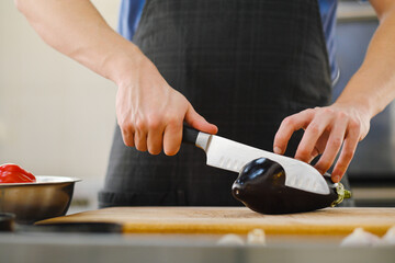 The male Caucasian chef cuts vegetables, peppers, tomatoes and eggplants on a wooden cutting board.