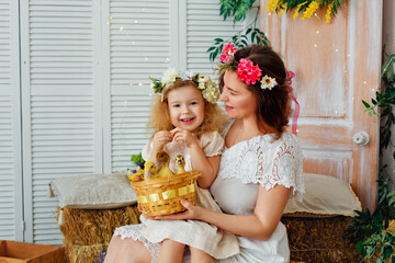 Easter composition. Mother and daughter in white dresses and flower wreaths on their heads play with ducklings. Farm village village holiday. Children and pets