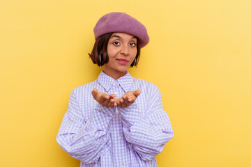 Young mixed race woman wearing a beret isolated on yellow background holding something with palms, offering to camera.