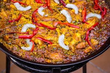 Close up background of tasty and Spanish typical seafood paella with prawns, peas, chicken and red pepper in a base of rice and vegetables. Traditional Spanish food. Paella cooked in a paella pan.