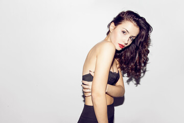 Fototapeta premium Front view of an attractive brunette young woman in black lengerie is possing and looking at camera on grey background.