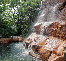 Close-up of powerful water falling into a pool from a large man-made waterfall in a green tropical garden