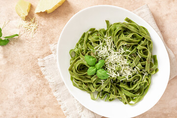 Spinach pasta with pesto sauce and grated cheese in a white plate on a light background top view. Italian food, Mediterranean cuisine. Green tagliatelle pasta with pesto and parmesan.