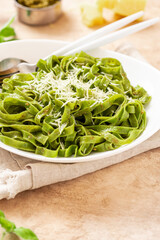 Spinach pasta with pesto sauce and grated cheese in a white plate on a light background. Italian food, Mediterranean cuisine. Green tagliatelle pasta with pesto and parmesan.