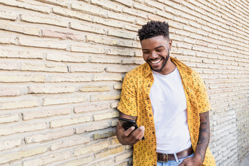 Lifestyle portrait of a handsome american man using a smartphone in the street with brick wall as background