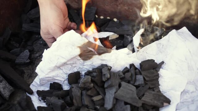 A young man lights a fire with paper matches and coals. Metal grill. Rest in nature, patio Bonfire for cooking barbecue