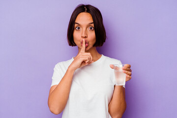 Young mixed race holding a glass of water isolated on purple background keeping a secret or asking...