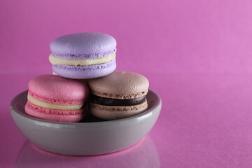 Macaroons three multicolored on a gray saucer plate stands on a pink background with a place for text and copyspace