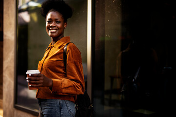 Young african woman outdoors. Beautiful woman with curly hair drinking coffee.