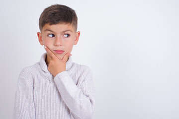 Caucasian kid boy wearing knitted sweater against white wall Thinking worried about a question, concerned and nervous with hand on chin.