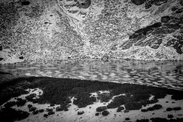 Monochrome view of mountain lake starting to freeze. Pieces of fresh ice floating on cold water of a lake in Tatra Mountains, Poland. Selective focus on the water, blurred background.