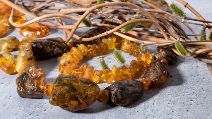 Dark orange and green old amber beads close up on a gray plastered background.  Ancient amber stone with plant inclusions, retro composition of amber jewelry and dry curved grapevine. 