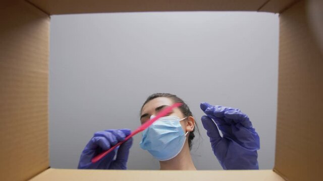 home delivery, shipping and pandemic concept - woman in protective medical mask and gloves unpacking parcel box with cosmetics and beauty products