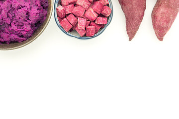 Purple yams whole, sliced square in a bowl, and mashed potatoes on the dish placed on a white background. Space for text. Purple sweet potatoes. Top view. Vegan fruit and healthy fruits concept
