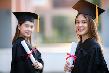 Young happy Asian woman university graduates in graduation gown and mortarboard hold a degree certificate celebrate education achievement in the university campus.  Education stock photo
