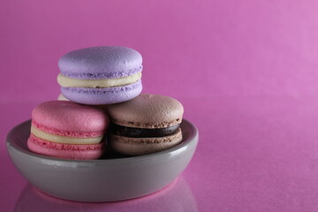 Macaroons three multicolored on a gray saucer plate stands on a pink background with a place for text and copyspace