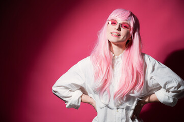 Close-up portrait of a young woman with braces in a pink wig and sunglasses on a pink background.
