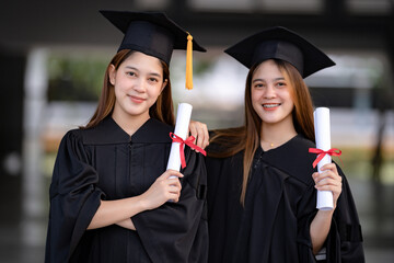 Young happy Asian woman university graduates in graduation gown and mortarboard hold a degree certificate celebrate education achievement in the university campus.  Education stock photo