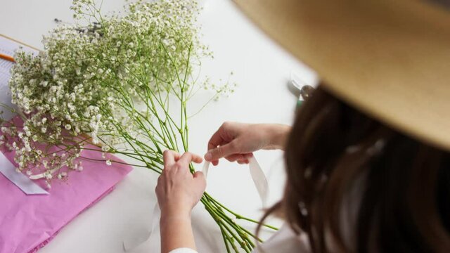 people, gardening and floral design concept - close up of woman arranging flowers and tying bow at home