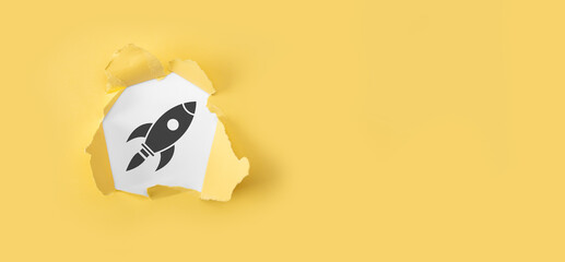 Torn yellow paper with rocket icon on white background.Start up concept with businessman holding abstract digital rocket icon rocket is launching and soar flying.Rapid growth concept