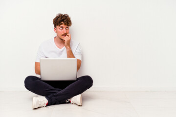 Young caucasian man sitting on the floor holding on laptop isolated on white background relaxed thinking about something looking at a copy space.