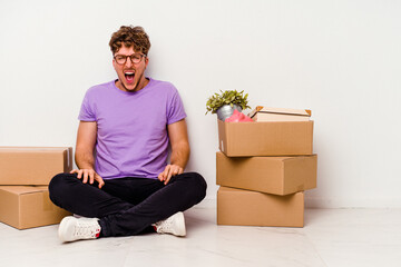 Young caucasian man sitting on the floor ready for moving isolated on white background screaming very angry and aggressive.