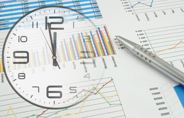 Business time concept. Pen on financial reports and clock.