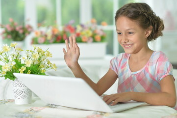 Emotional cute girl using laptop at home waving hand