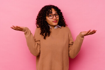 Young mixed race woman isolated on pink background doubting and shrugging shoulders in questioning gesture.